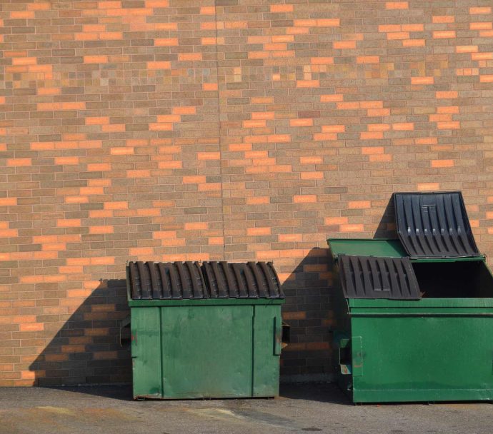 Green recycling dumpsters against a brick wall
